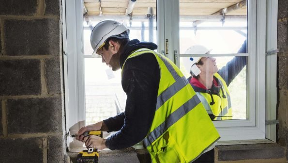 A workman on a construction site, builder in hard hat using an electric drill on a window sill.